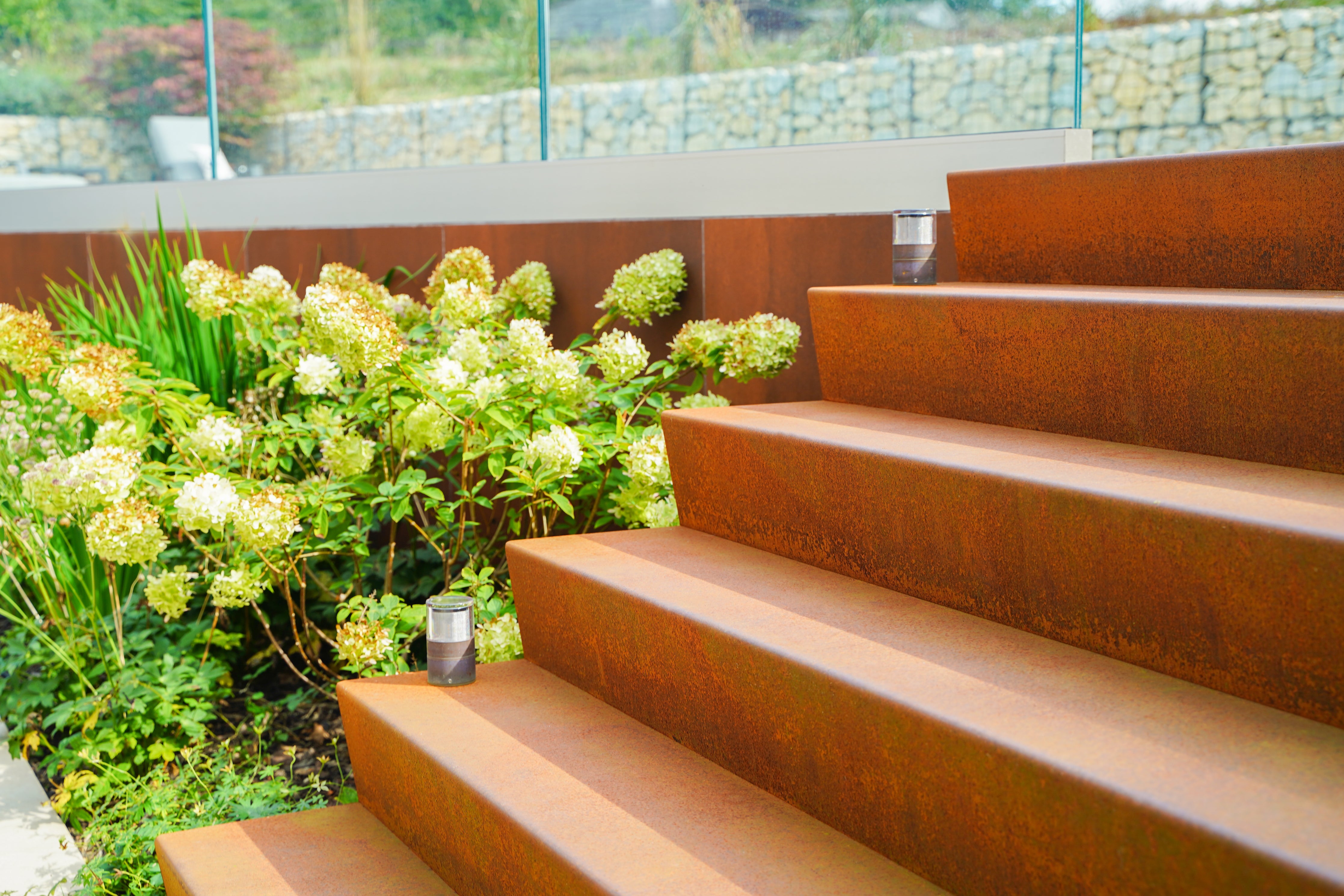 Corten steel garden staircase leading to a raised terrace. There is a large white hydrangea plant next to the steps.