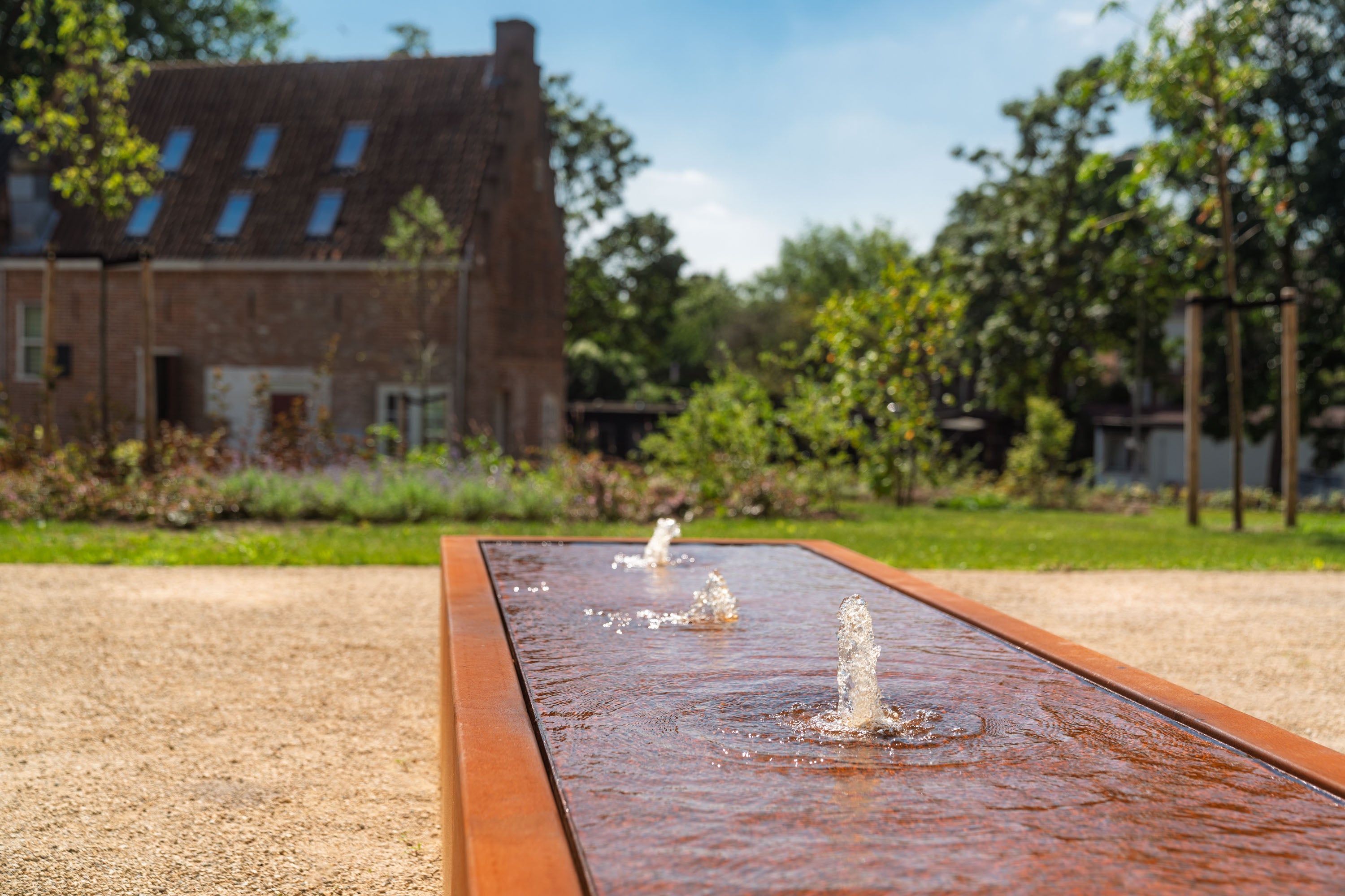 Fountain in a garden with a house and trees in the background