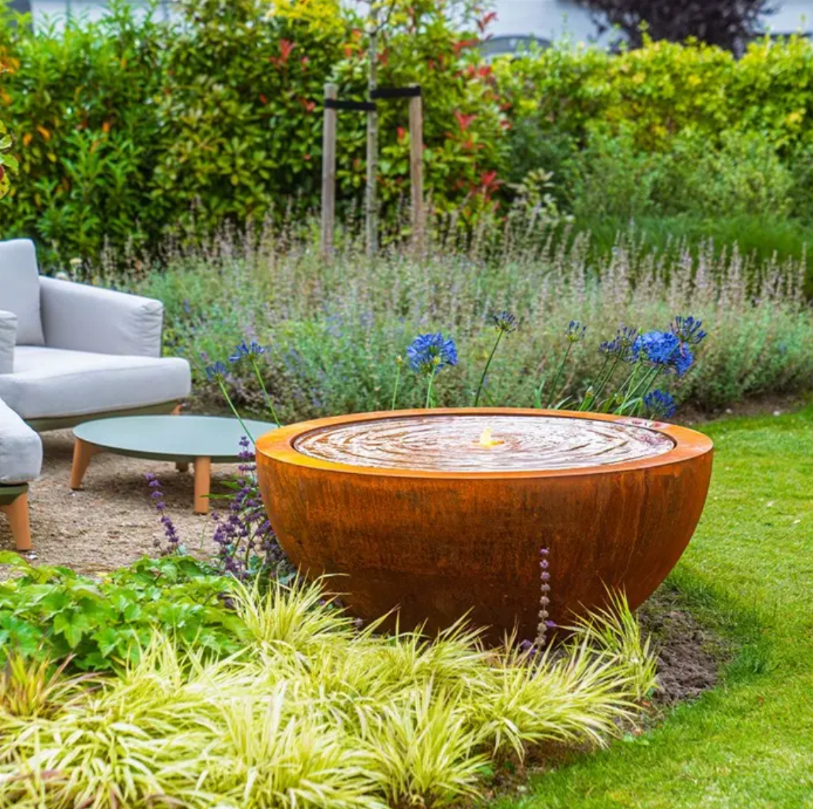 Outdoor garden setting with a water bowl surrounded by greenery and seating area.