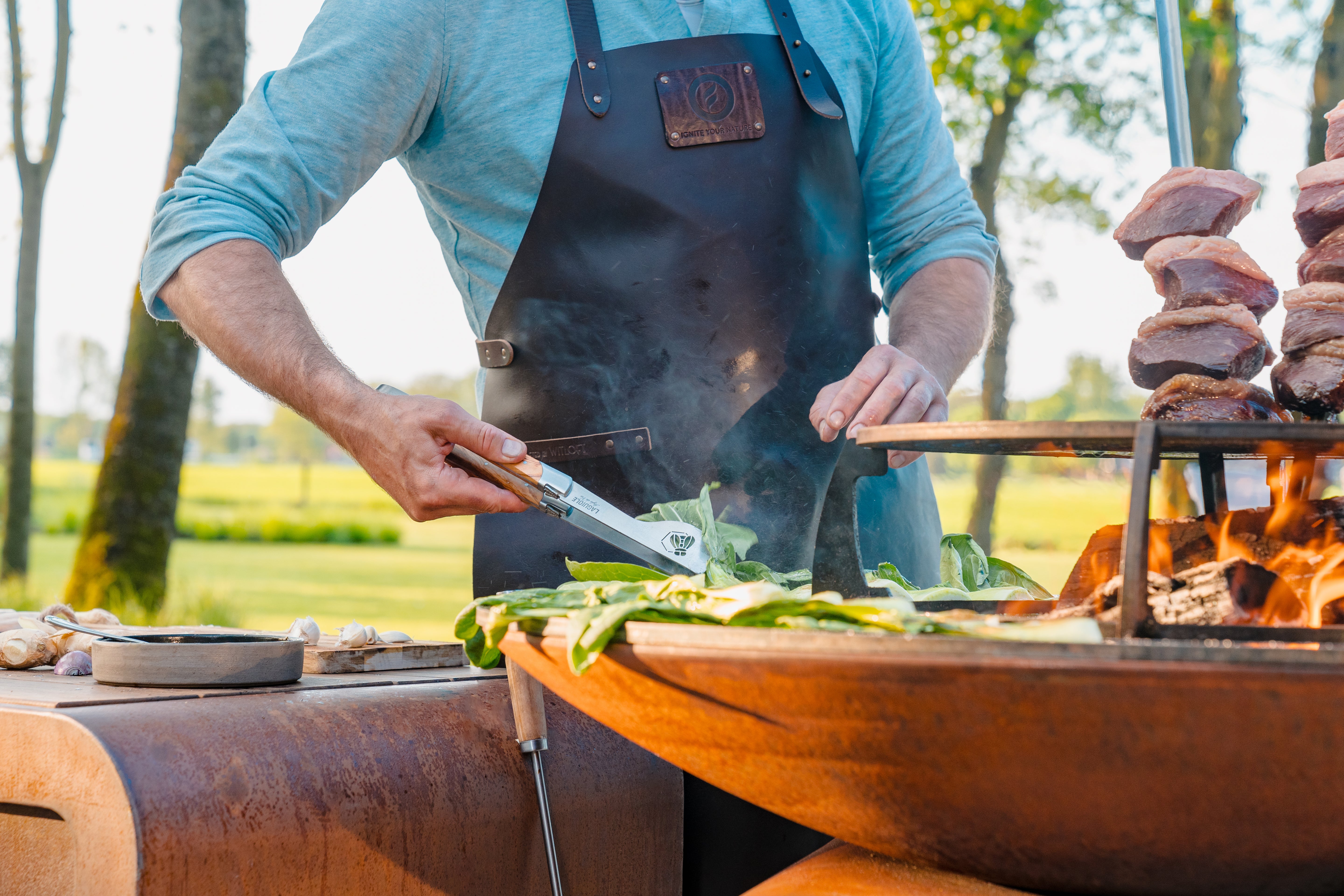 person cooking in a leather apron next to a lit bbq