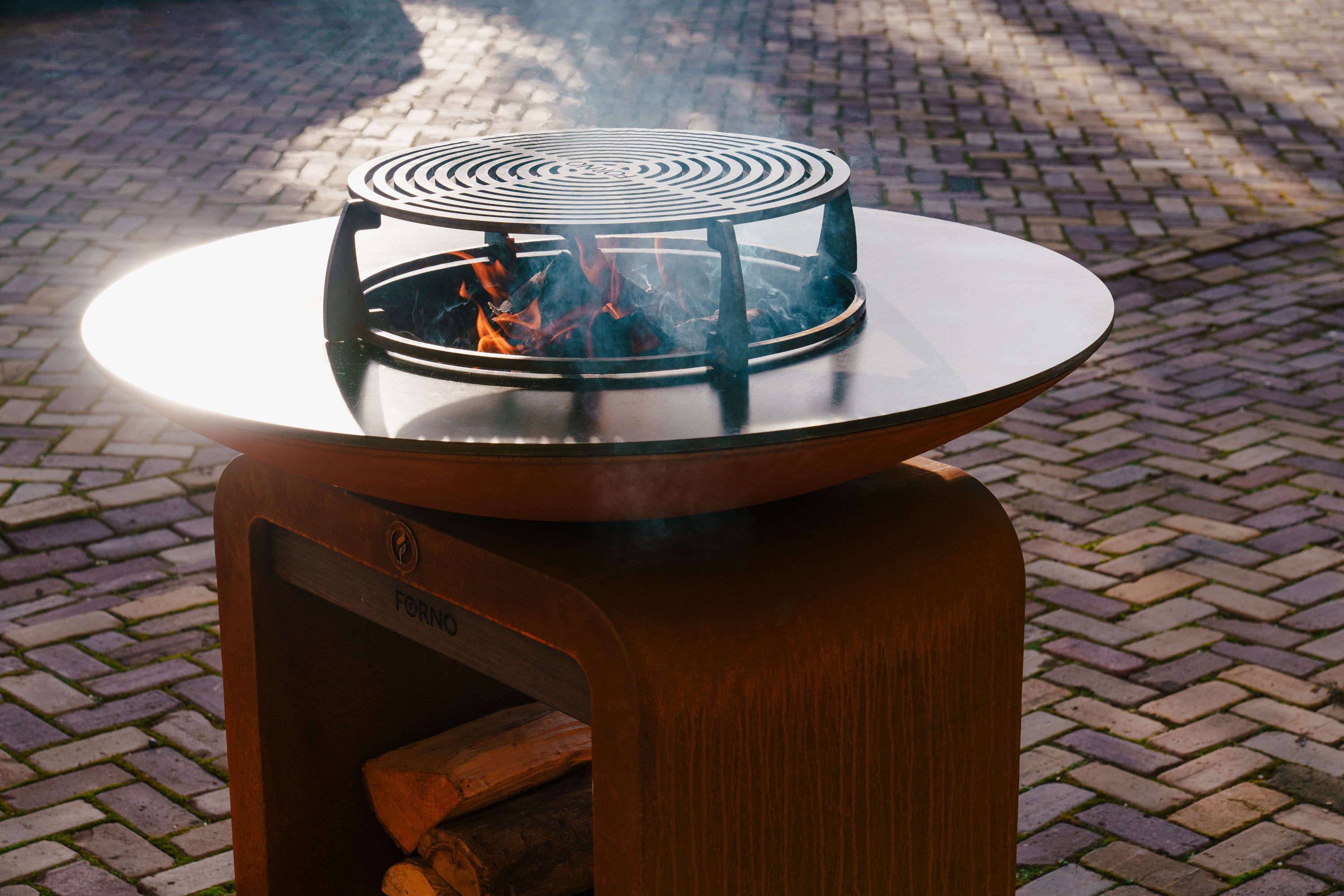 Outdoor fire pit table with burning logs on a brick patio