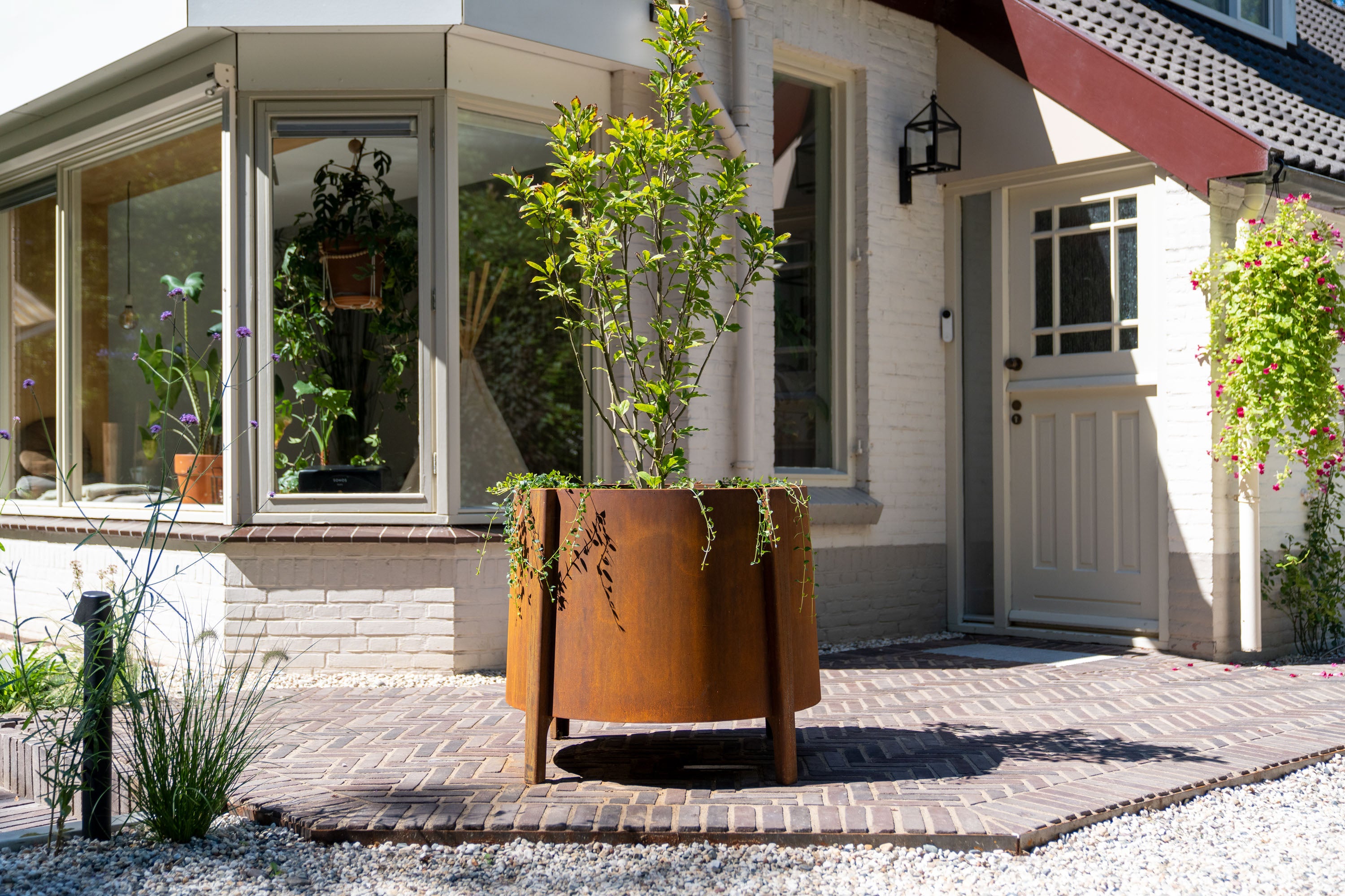 corten planter with feet planted with a tree on paving outside a house