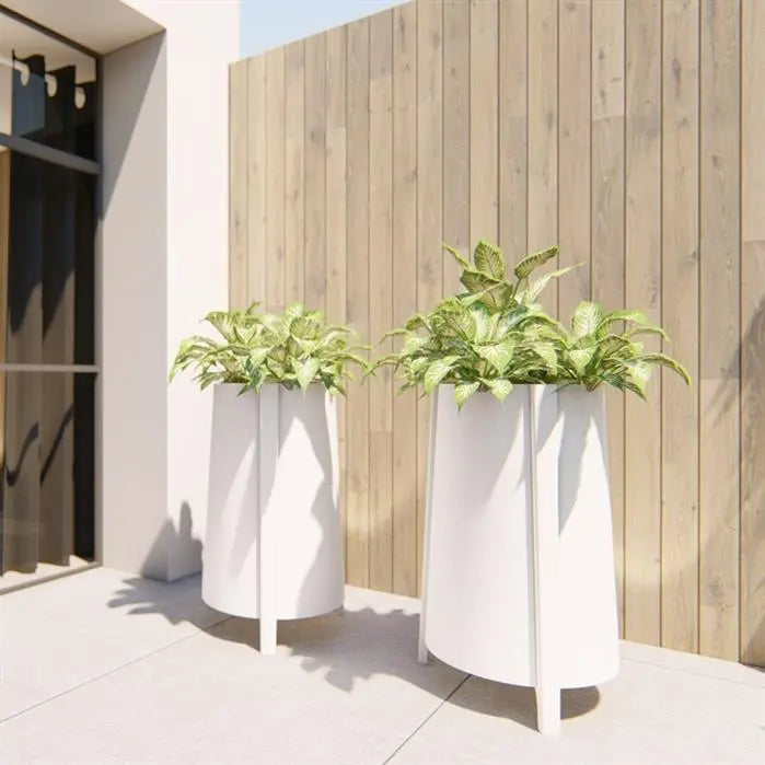 two tall white planters wit feet planted with greenery next to wooden fence