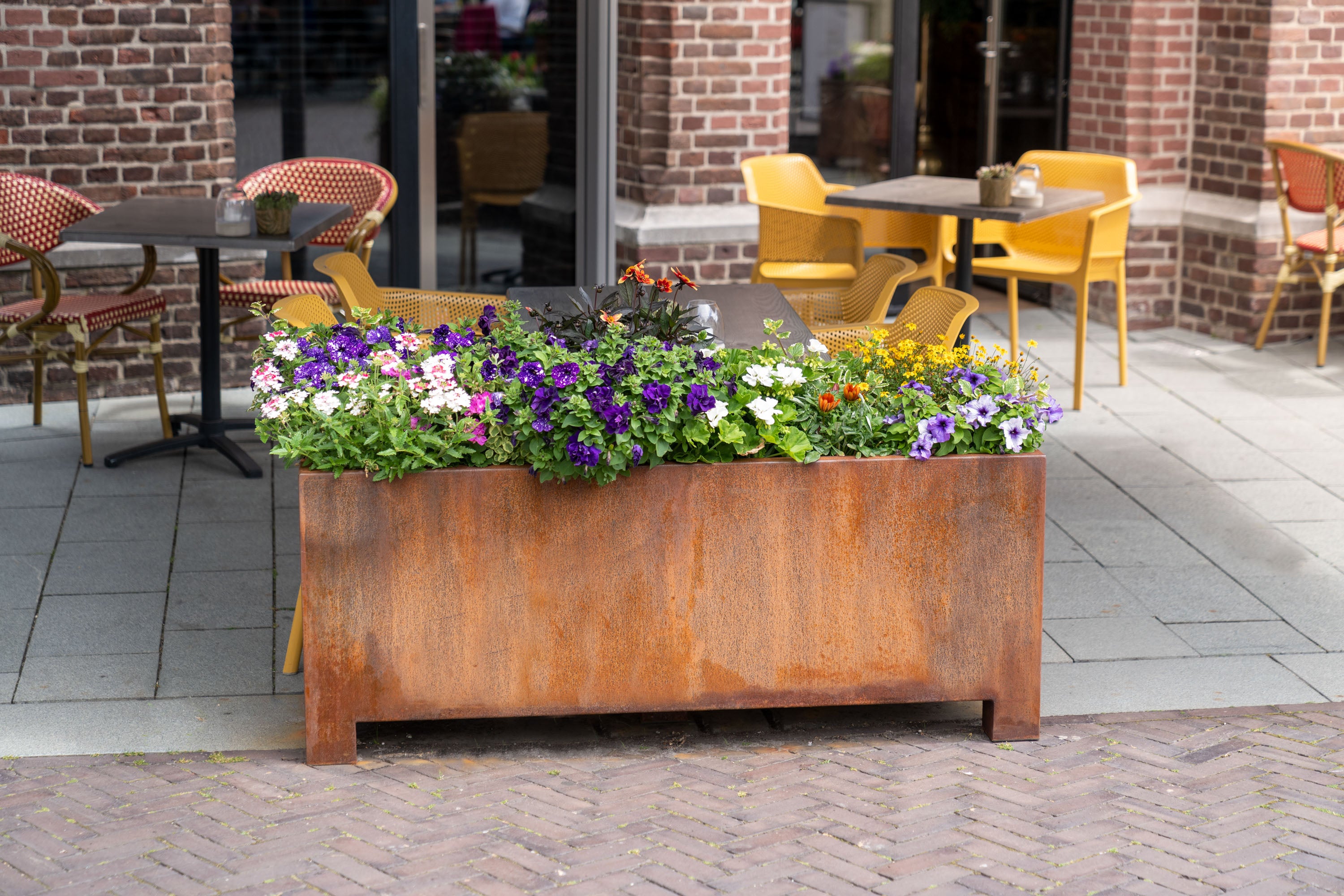 Corten steel planter with flowers on a patio with tables and chairs.