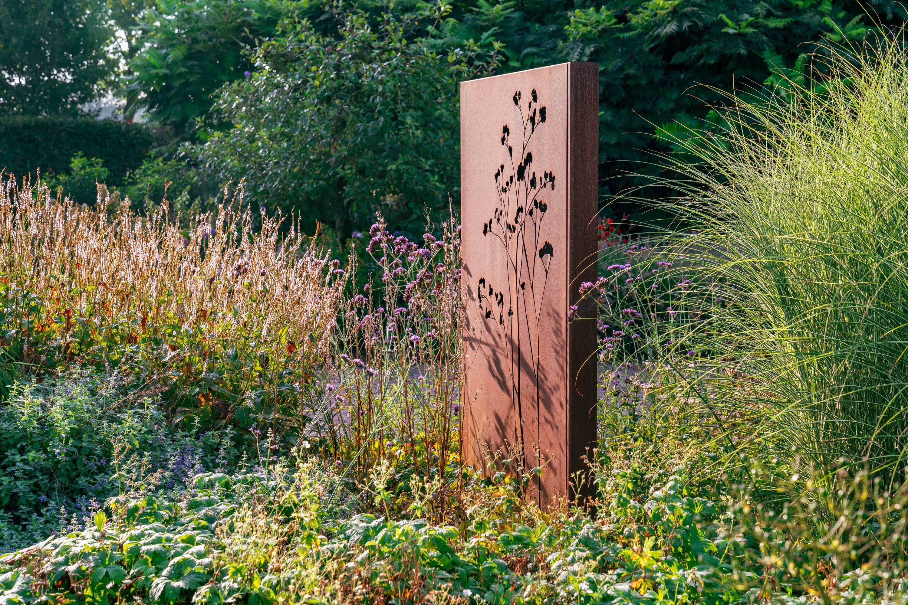 Metal sculpture in a garden setting with tall grasses and plants