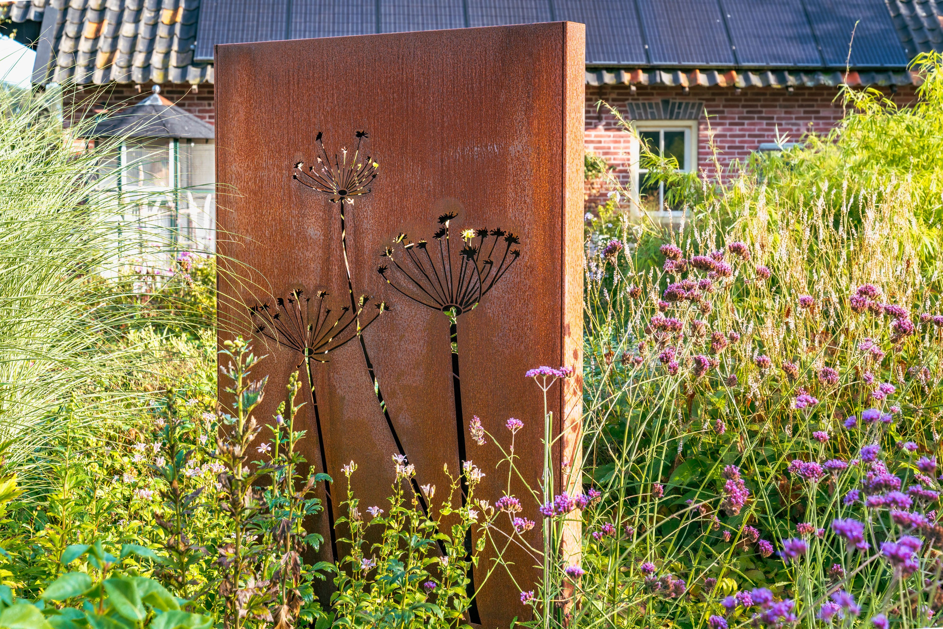 Corten steel art piece with floral design in a garden setting