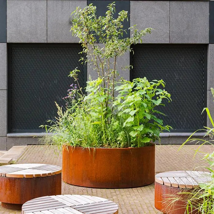 round corten steel planter with wheels planted up and situated in a courtyard