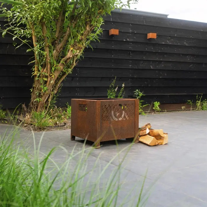 Corten steel planter box with decorative cutouts on a patio area in front of a black wooden wall.