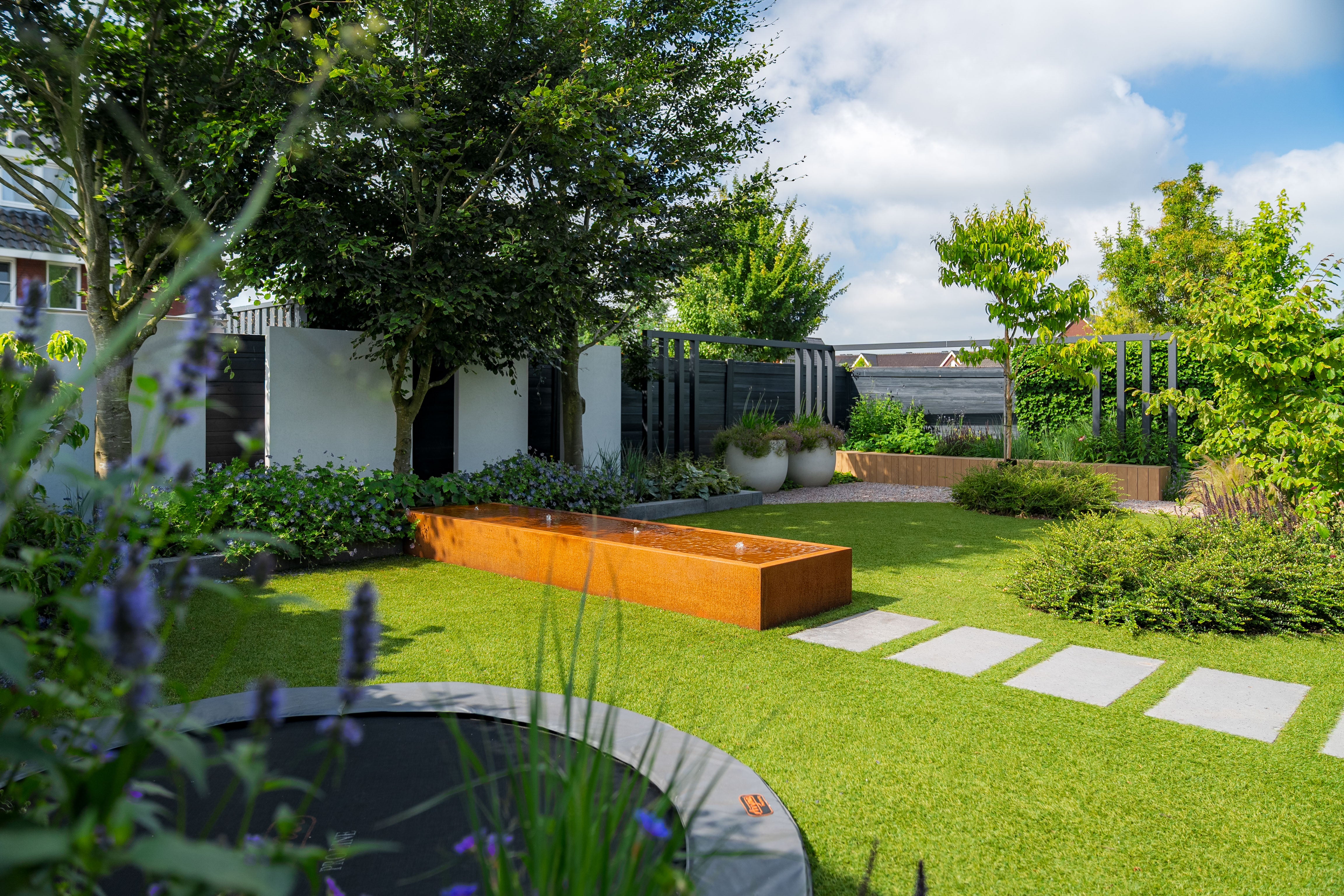 Modern garden with a water feature, paved area, and trees on a sunny day.