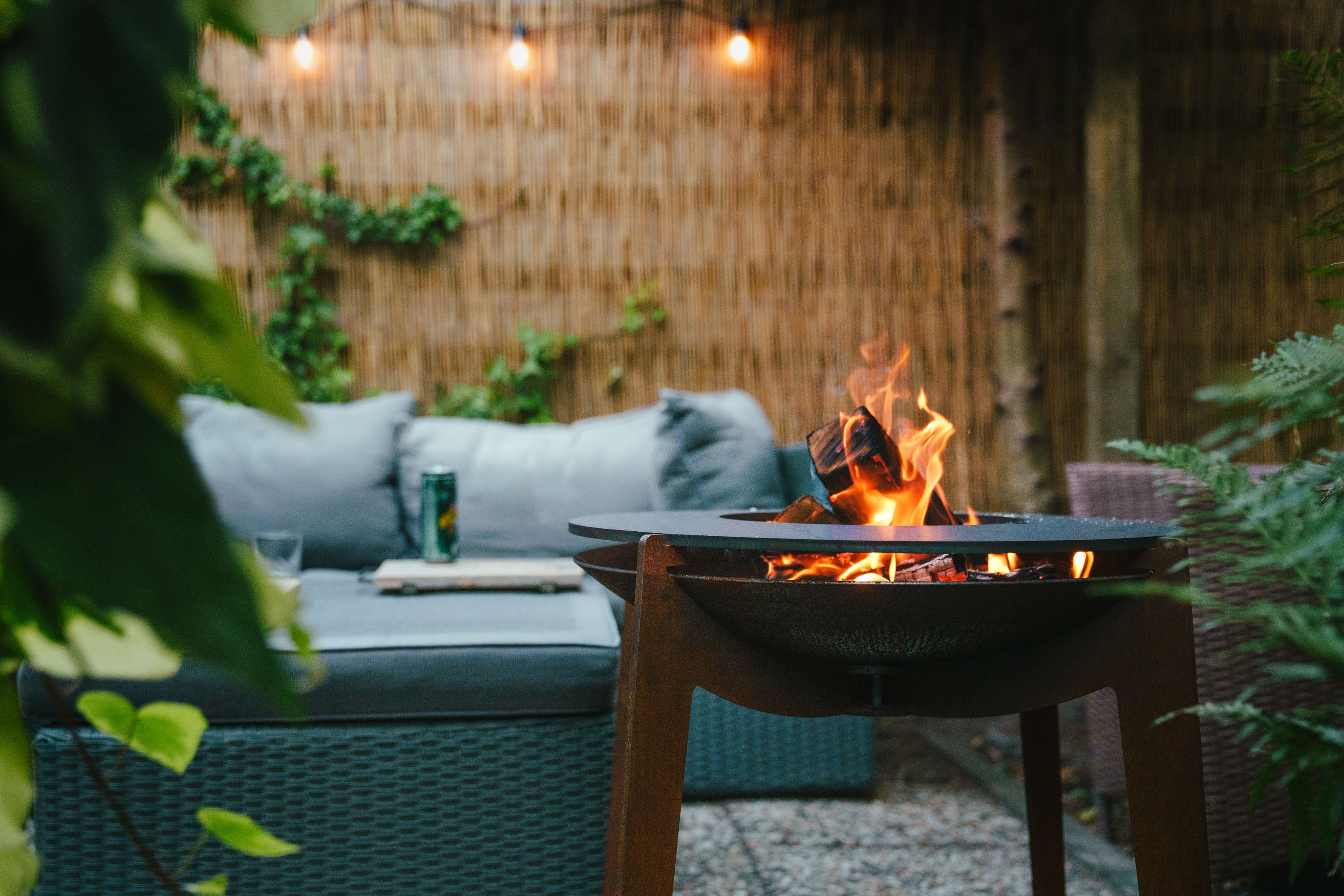 Fire pit table with flames in a backyard setting with outdoor furniture and plants.