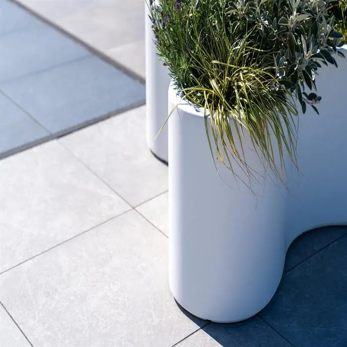 curvy white planter on paving with plants
