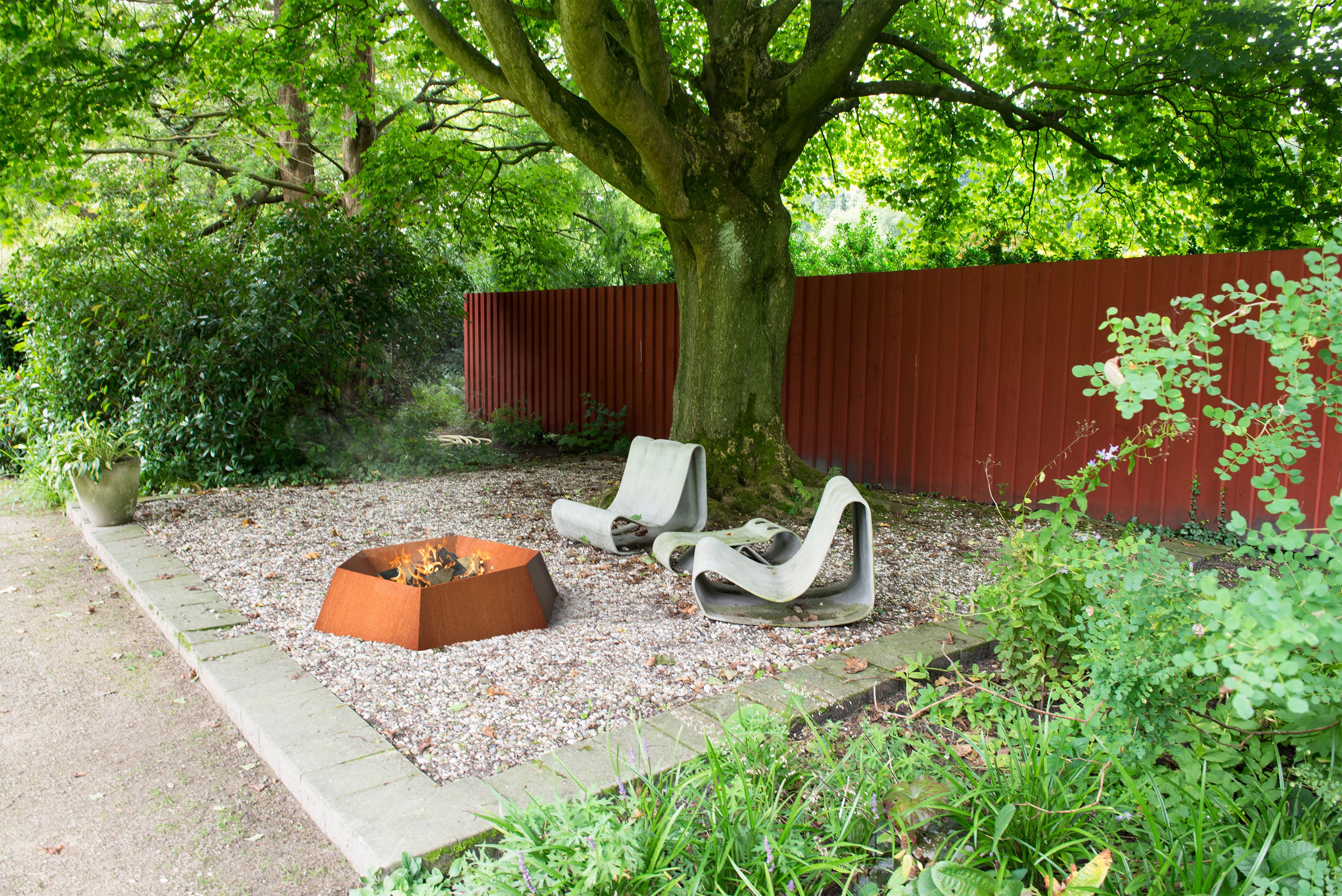 Garden setting with a fire pit, chairs, and a red fence.