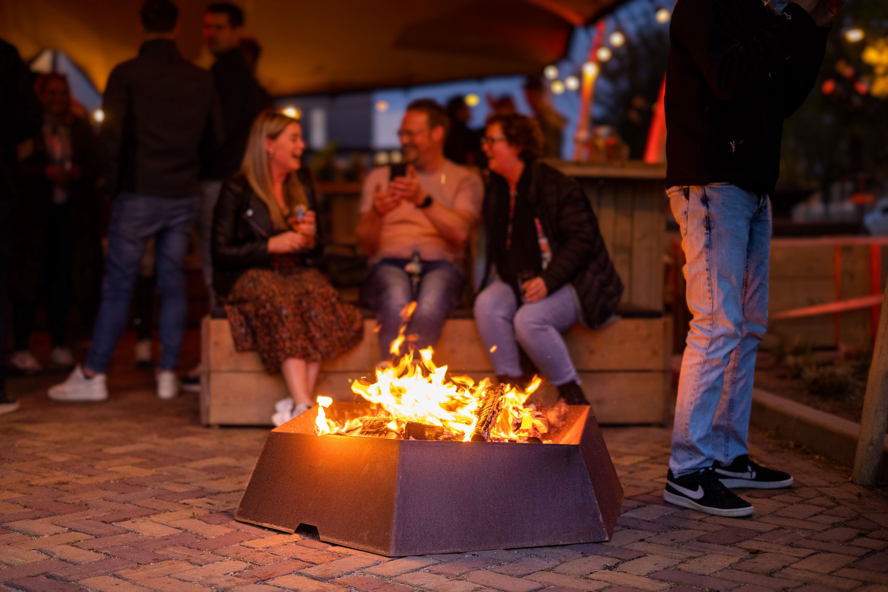 People gathered around a fire pit at night, with warm lighting and a casual atmosphere.