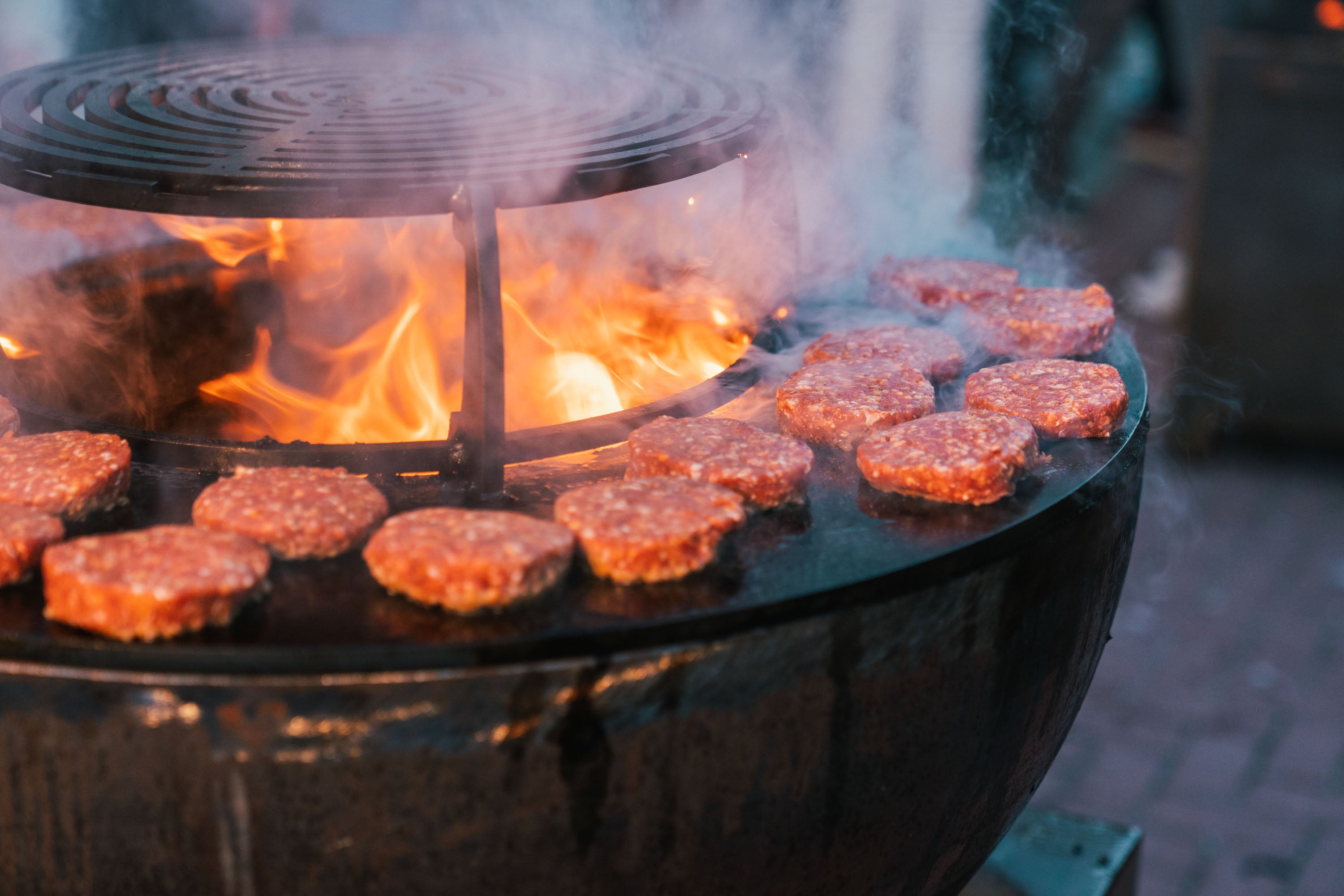 Hamburgers cooking on a grill over an open flame