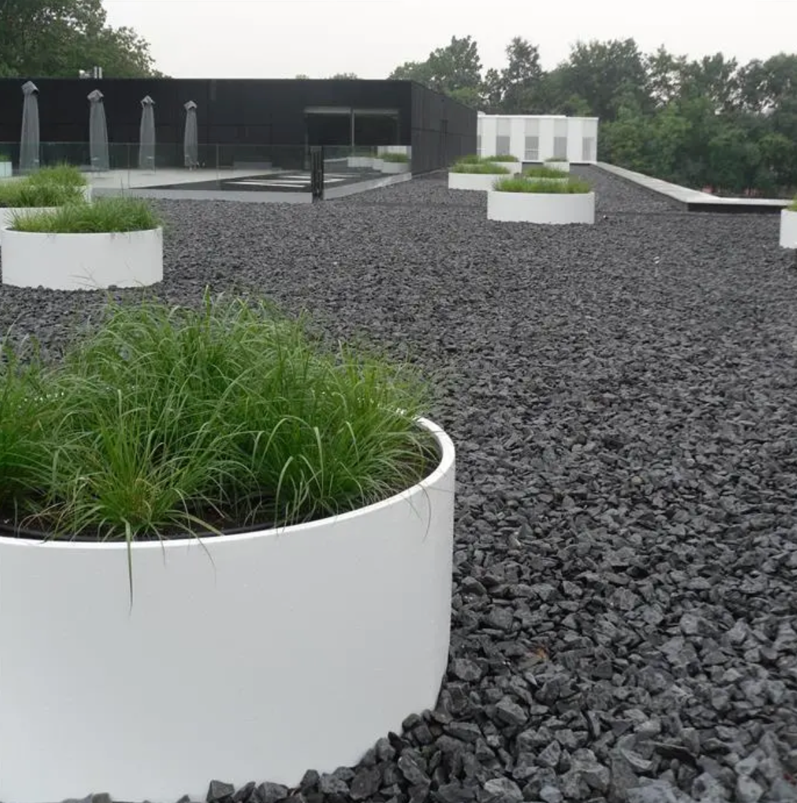 large white round planter in grey gravel planted with greenery
