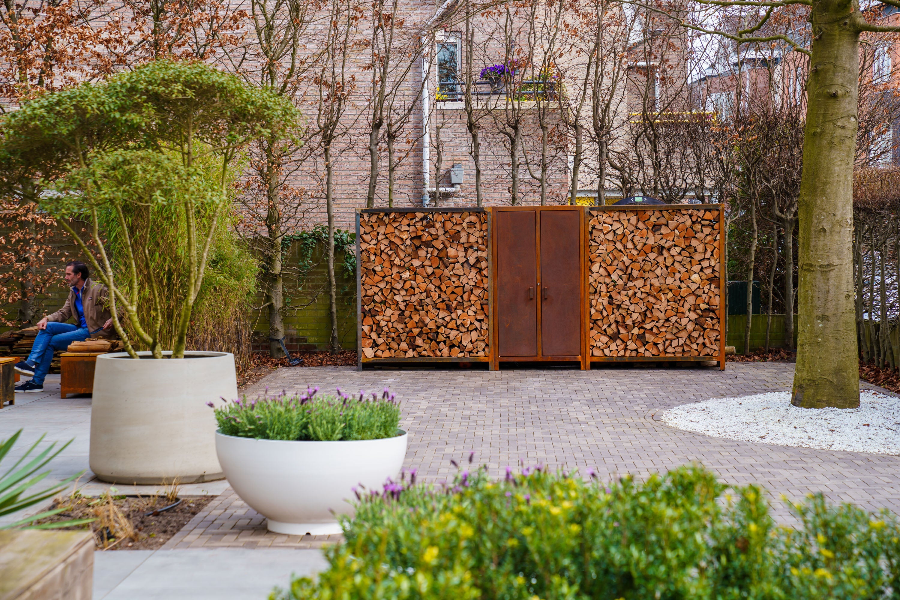 Outdoor setting with a wooden firewood storage unit, plants, and a bench.