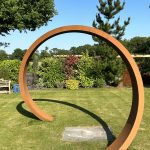Large metal circular sculpture in a garden setting