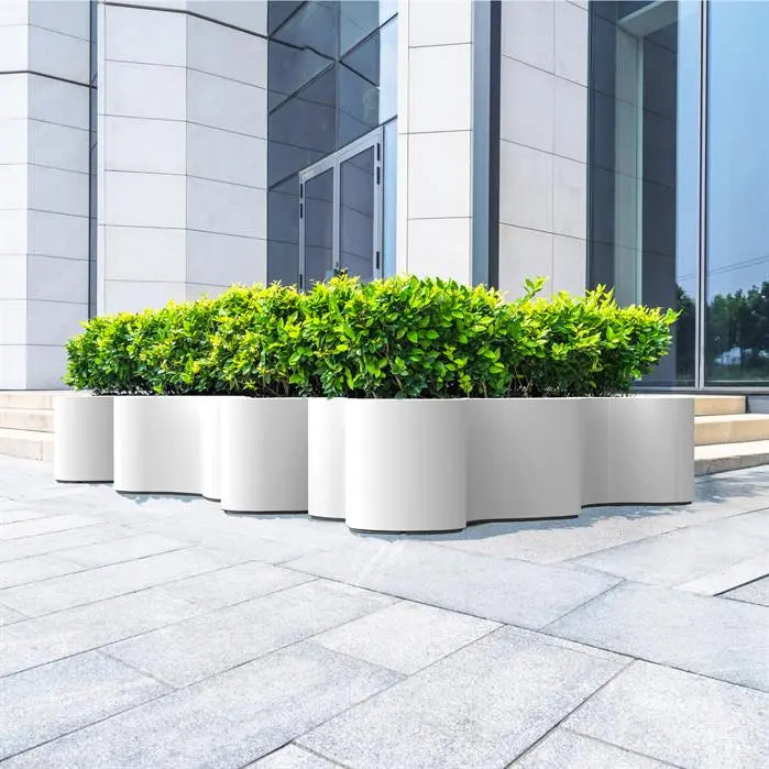 large curvy white planter outside a commercial building planted with shrubs