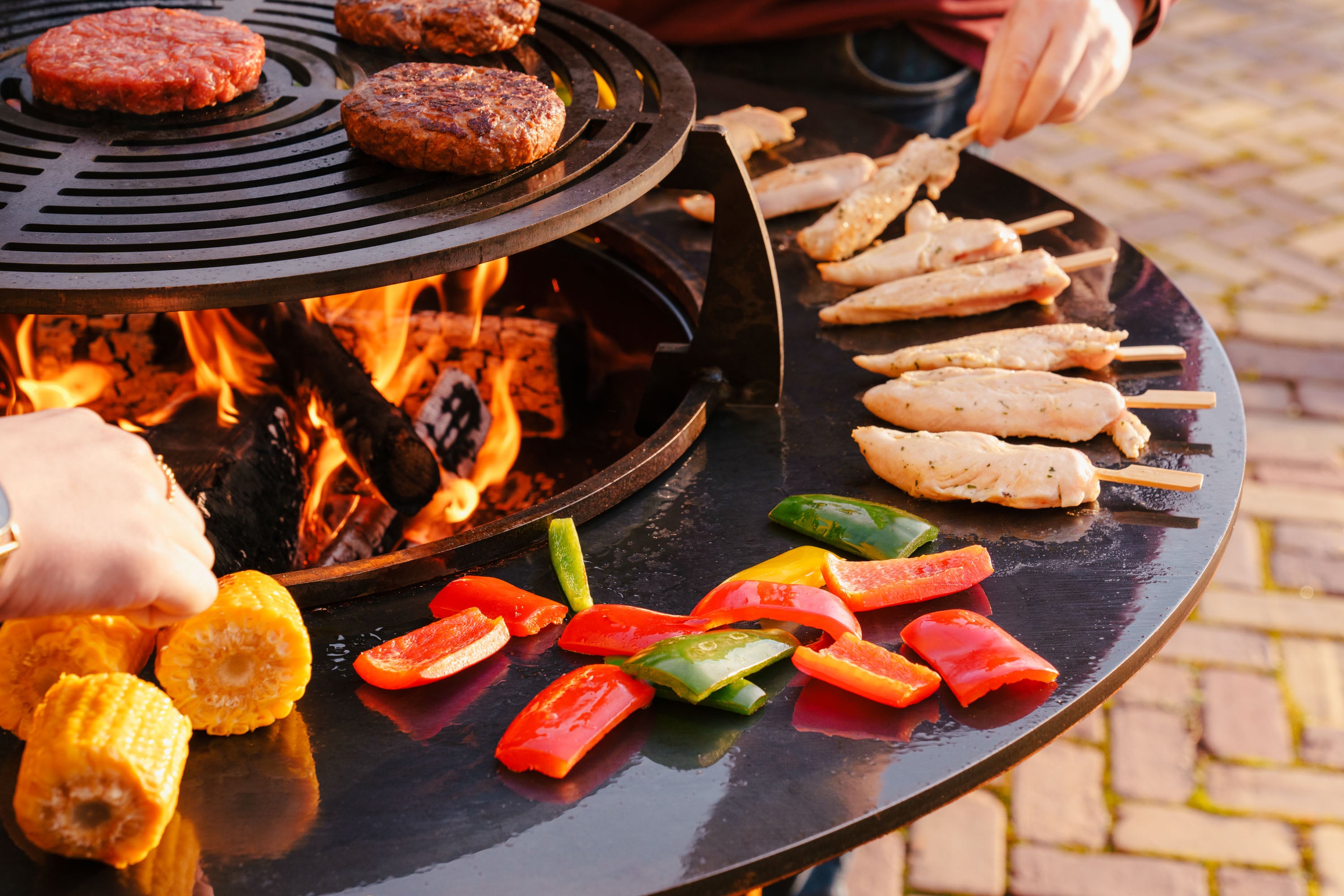 Outdoor cooking scene with grill, vegetables, and skewers on a brick patio.