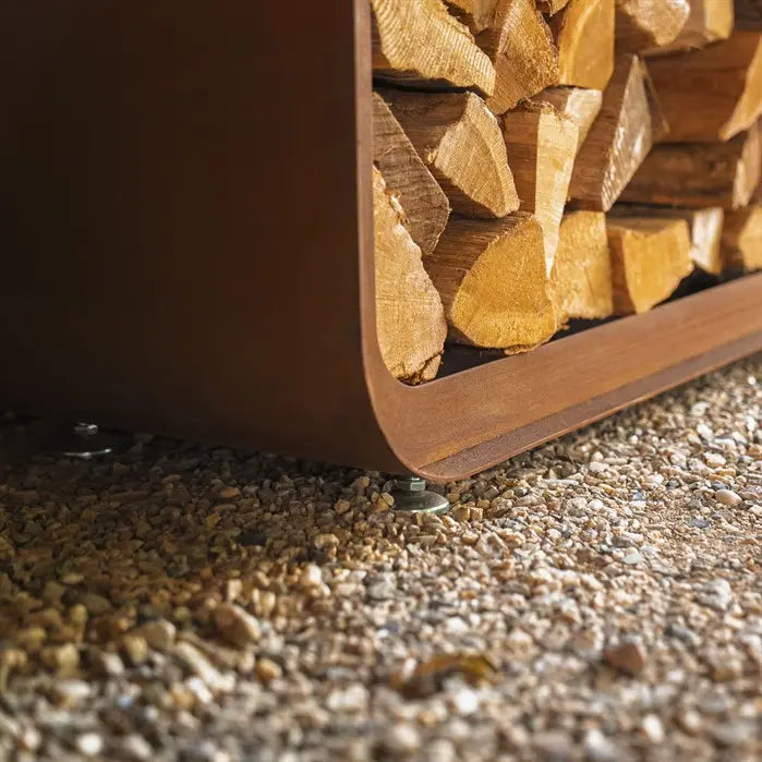Stack of firewood in a wooden holder on a gravel surface
