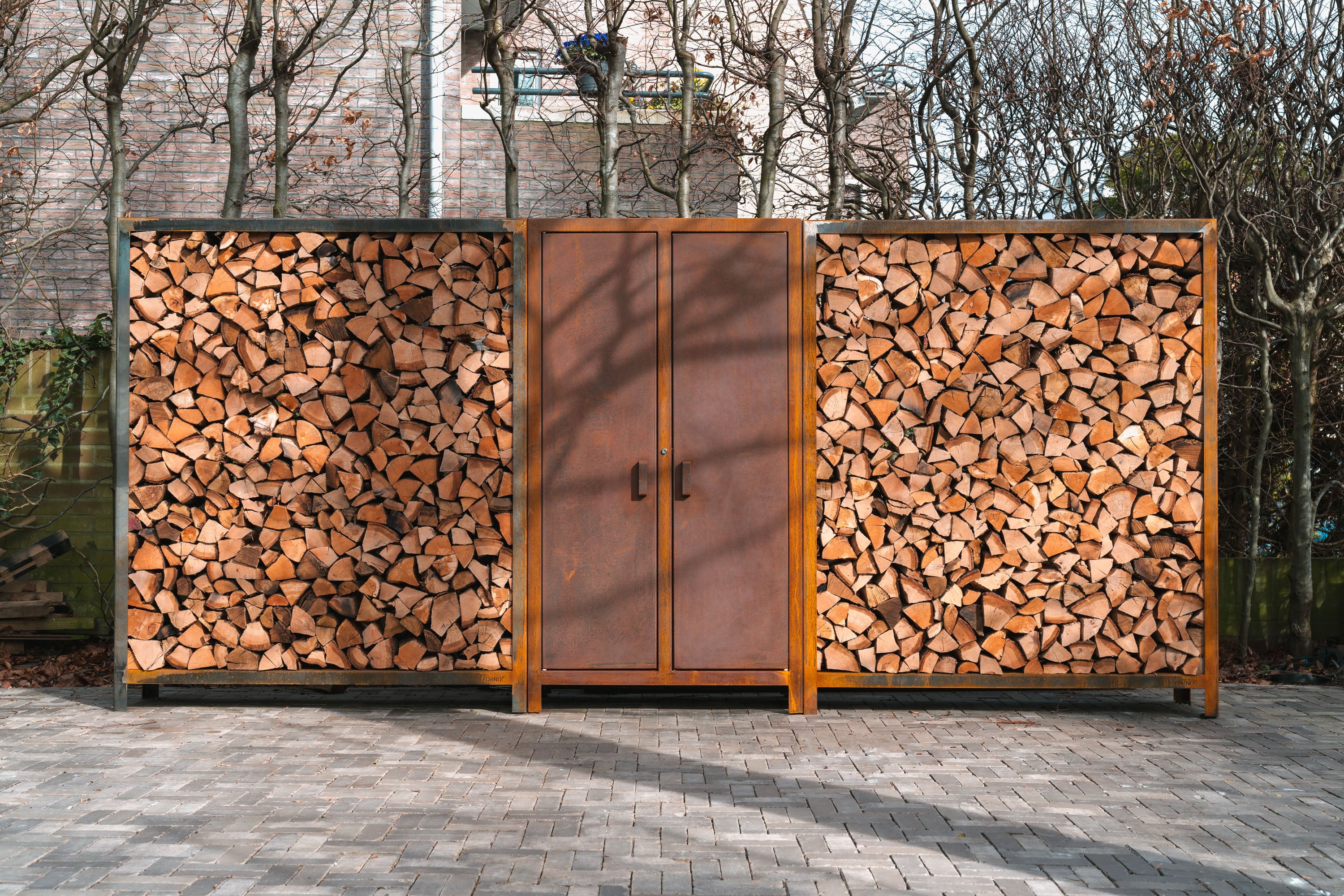 Wooden cabinet with firewood storage on a paved area with trees in the background