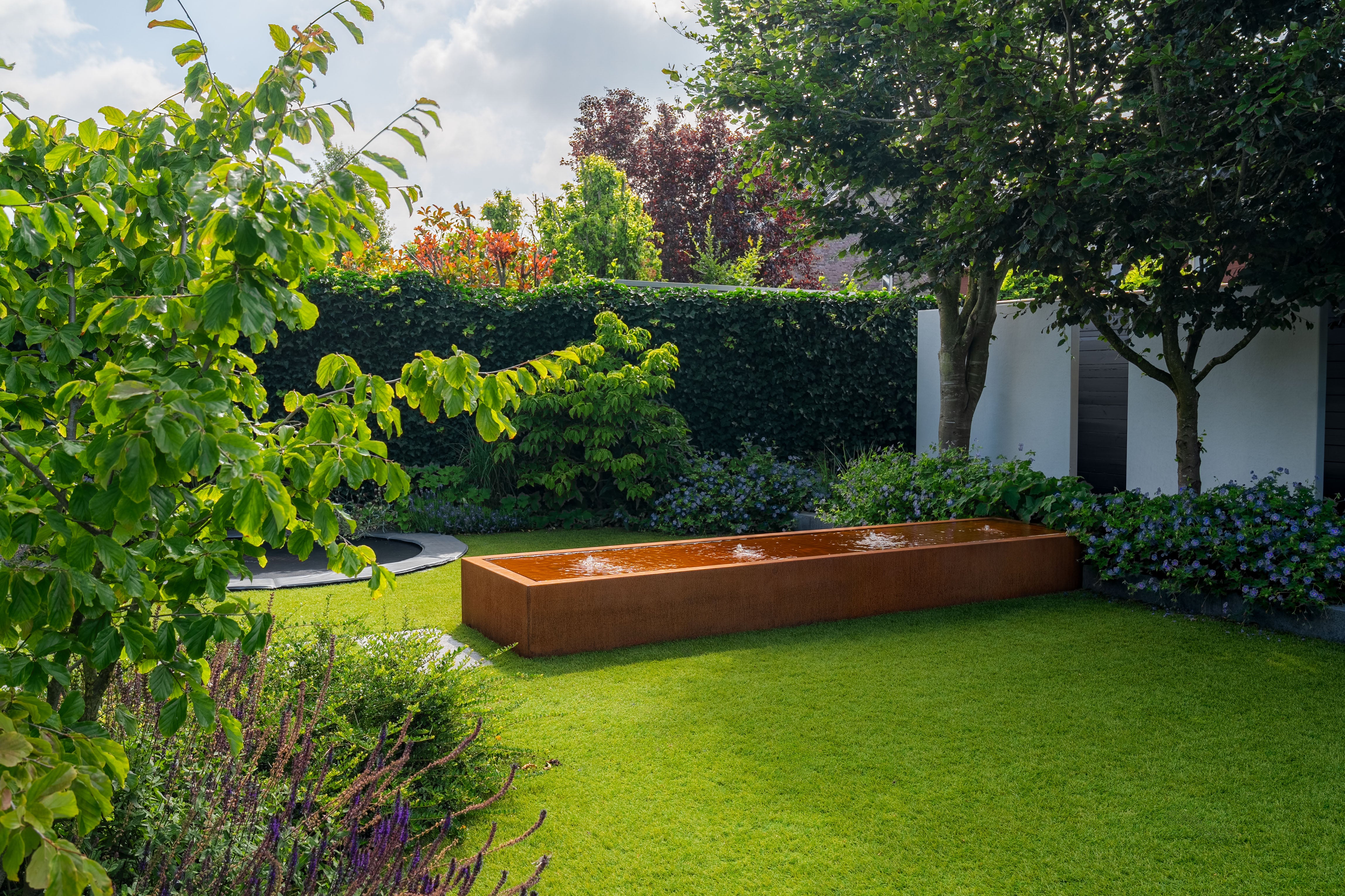 Garden with a rectangular water feature, green grass, and trees.