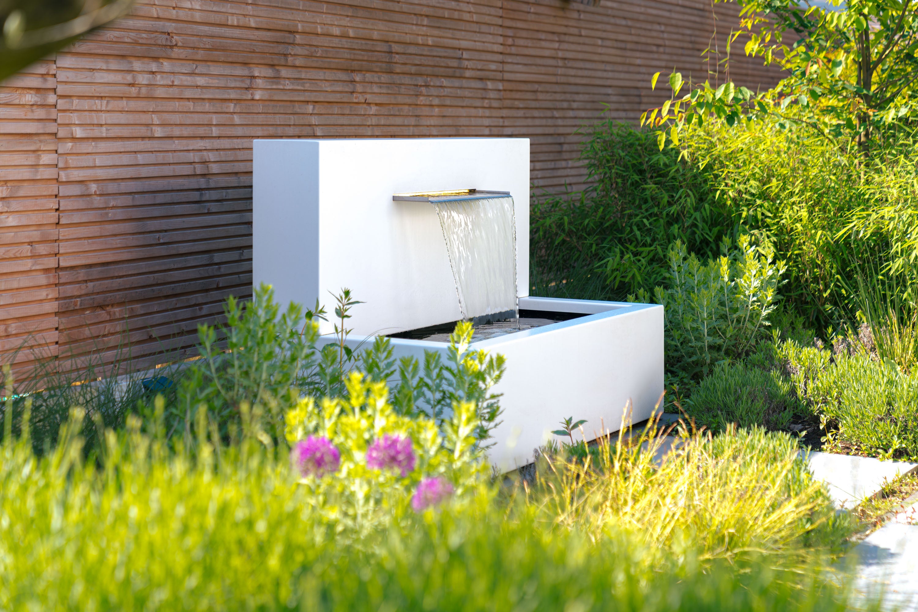 Modern outdoor fountain in a garden setting with wooden wall and greenery
