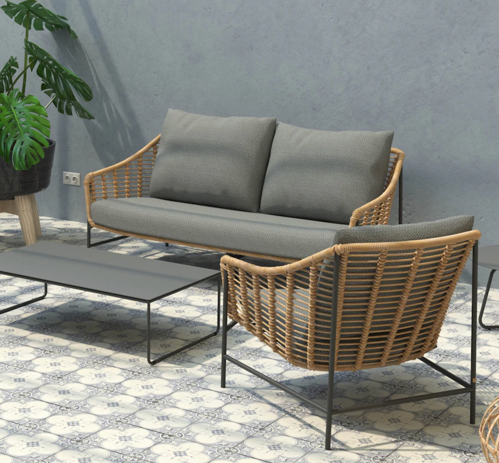 wicker style outdoor garden sofa & chair with grey cushions surrounding a  low black table. Set on tiled patio area