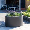 black ellipse shaped fibreglass planter on patio and planted with flowers