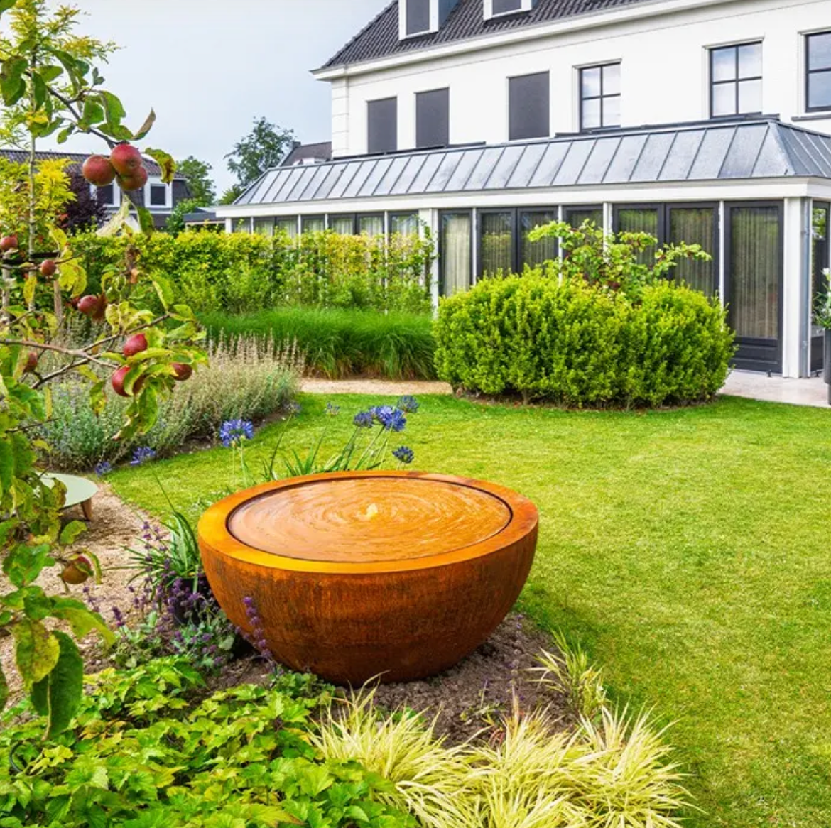 Decorative corten water feature in a garden with a house in the background