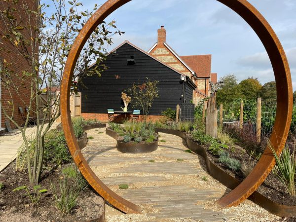 Garden pathway with circular metal frame, black building, and plants.