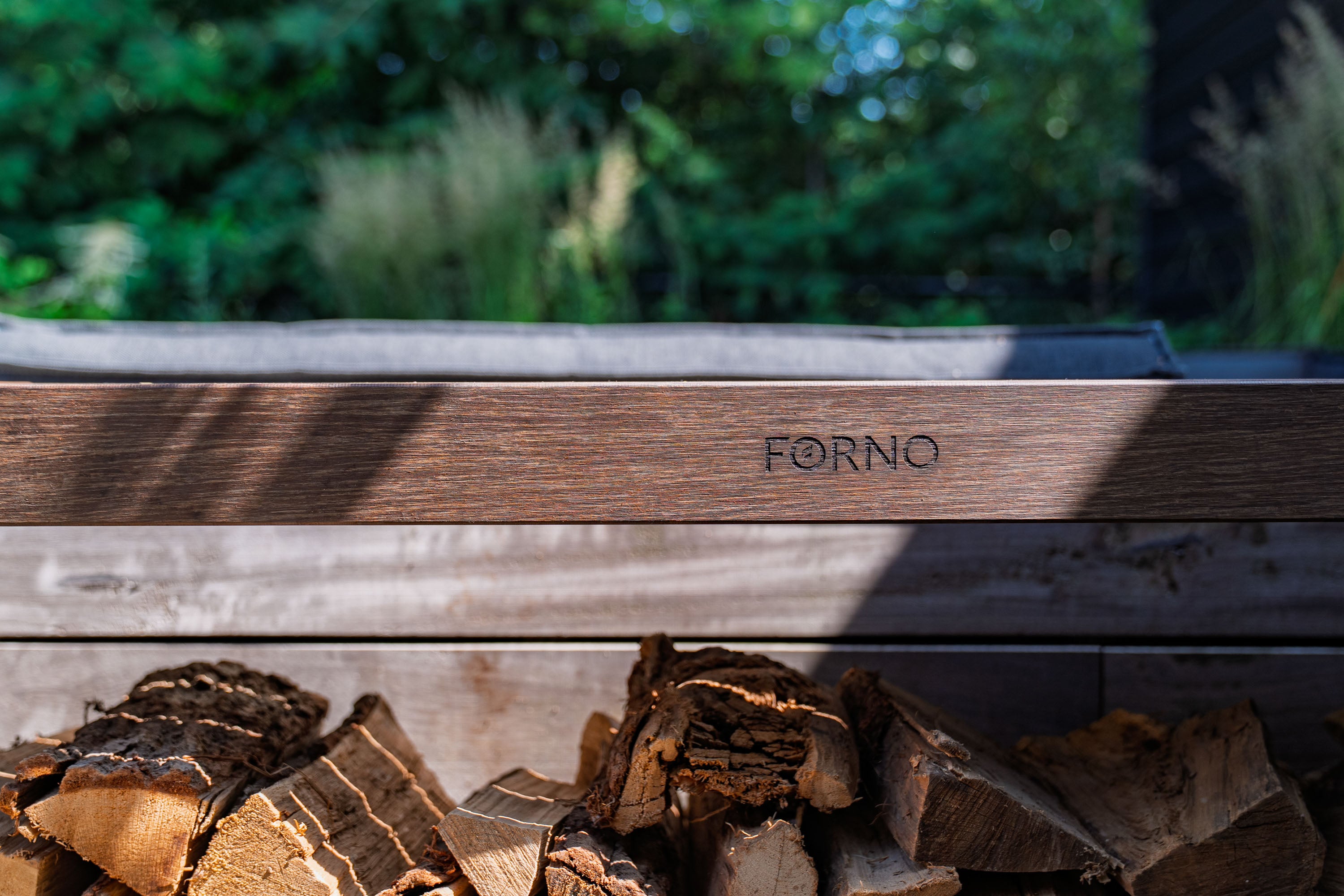 Wooden firewood with 'Forno' branding against a blurred green outdoor background