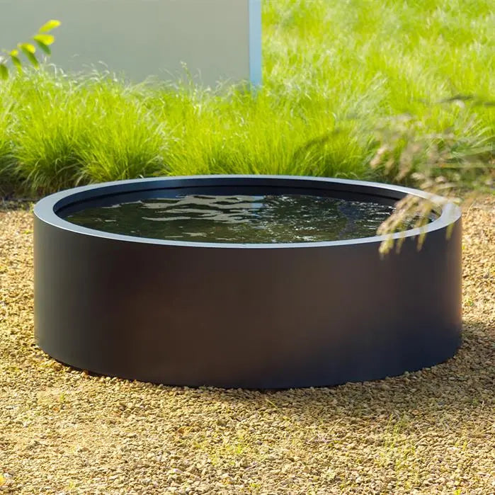 round black pond filled with water and sitting on gravel in front of grasses