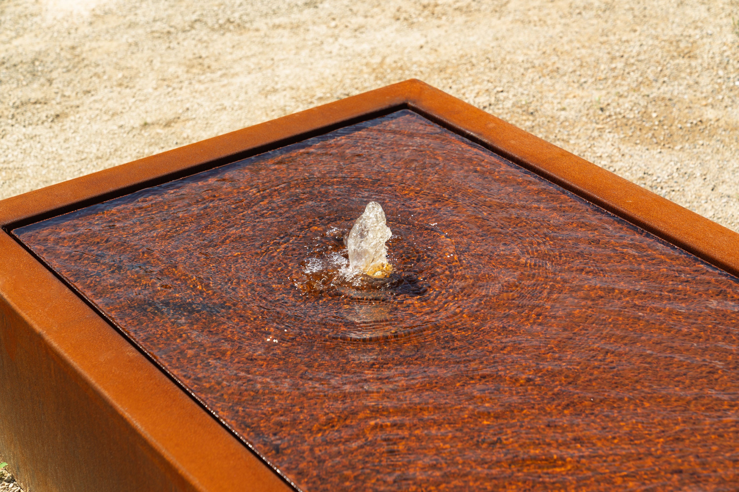 Rust-colored metal water feature with water fountain on a beige background