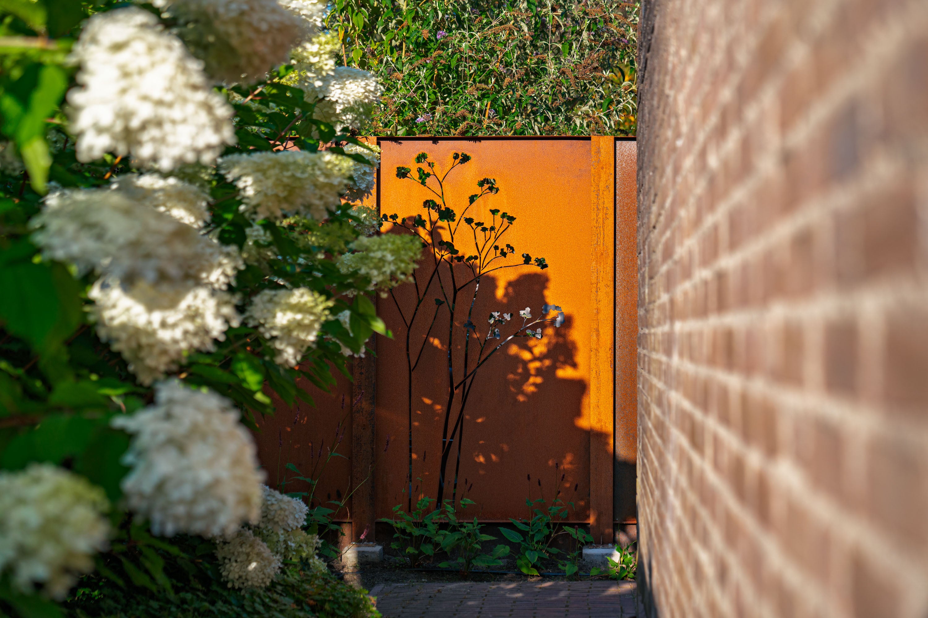 Orange metal gate with white flowers and a brick wall in the background