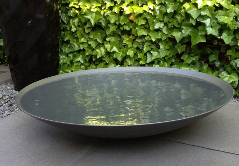 Large round metal bowl on a stone surface with green foliage in the background