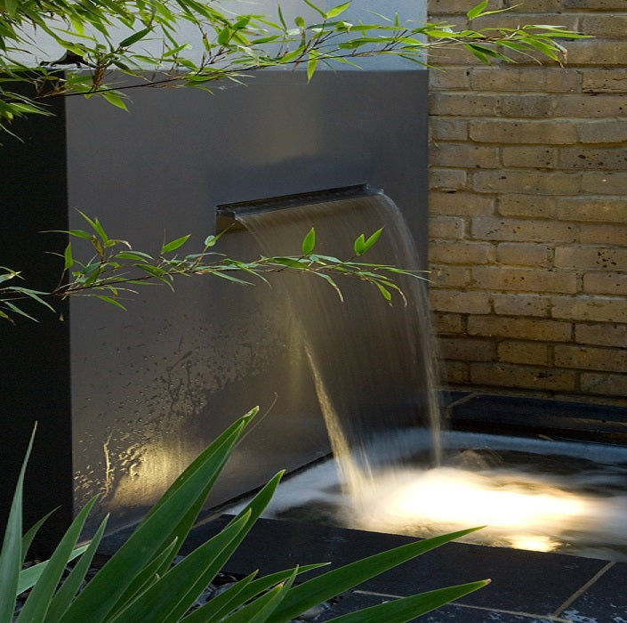 Waterfall feature with water flowing into a pool next to a brick wall