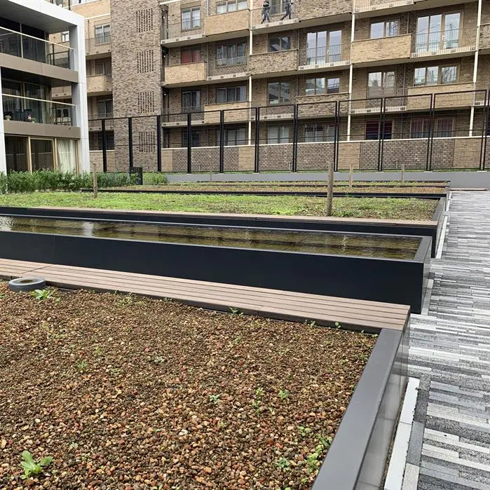 row of black beds and pond in public space with block of flats surrounding