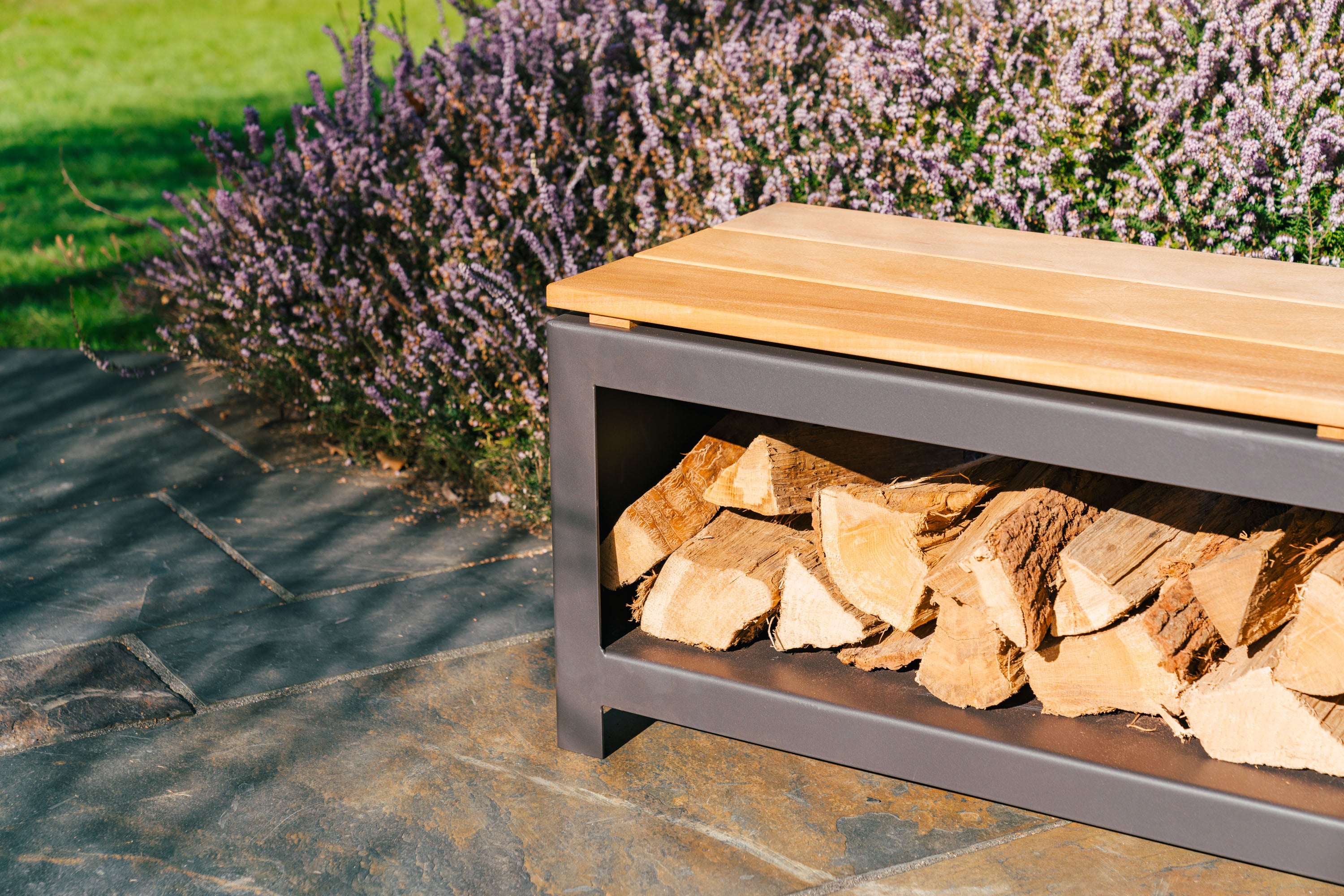 filled black wood storage bench with wooden top on paving net to flowering bush