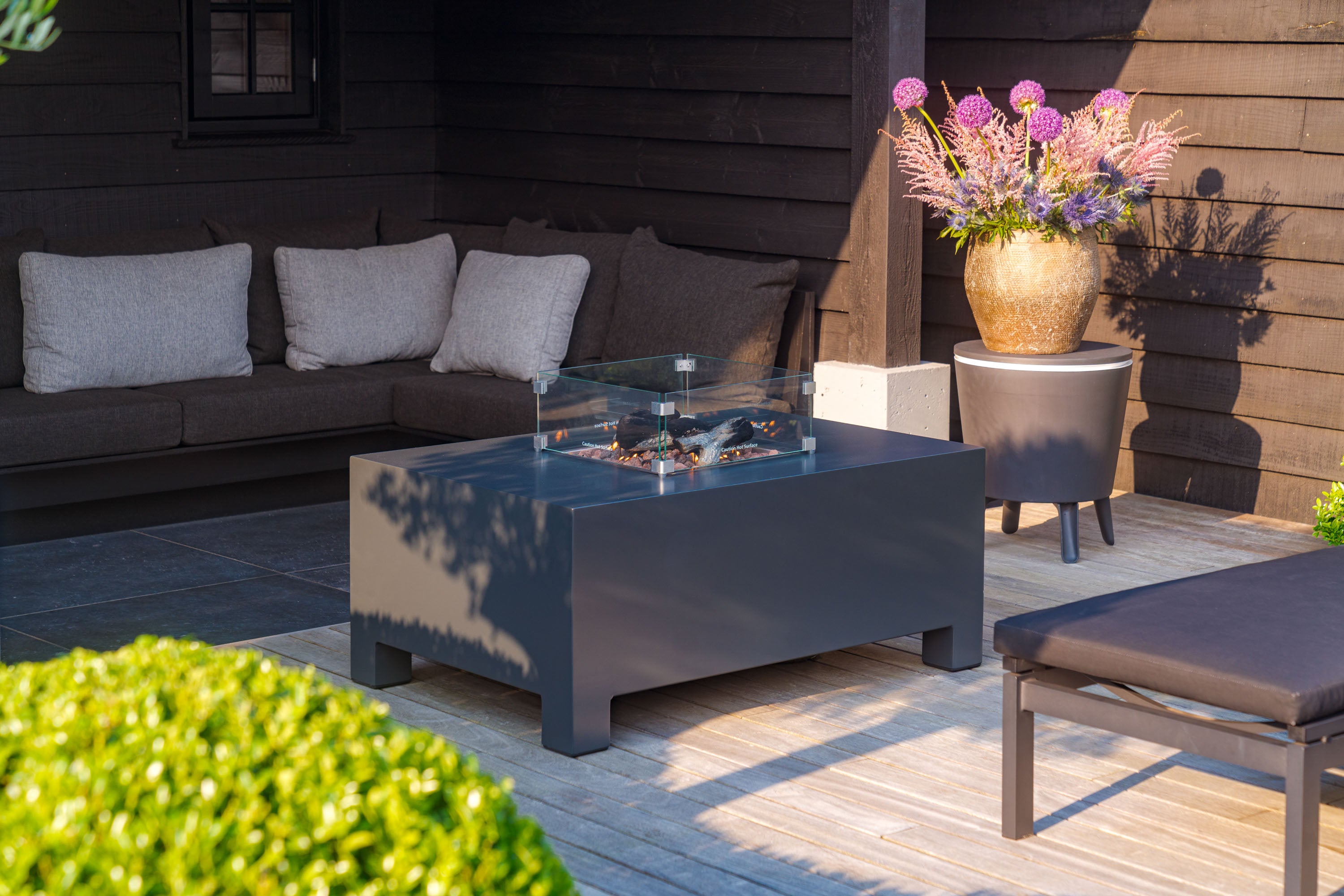 black gas fire table alight on decking next to sofa and plants