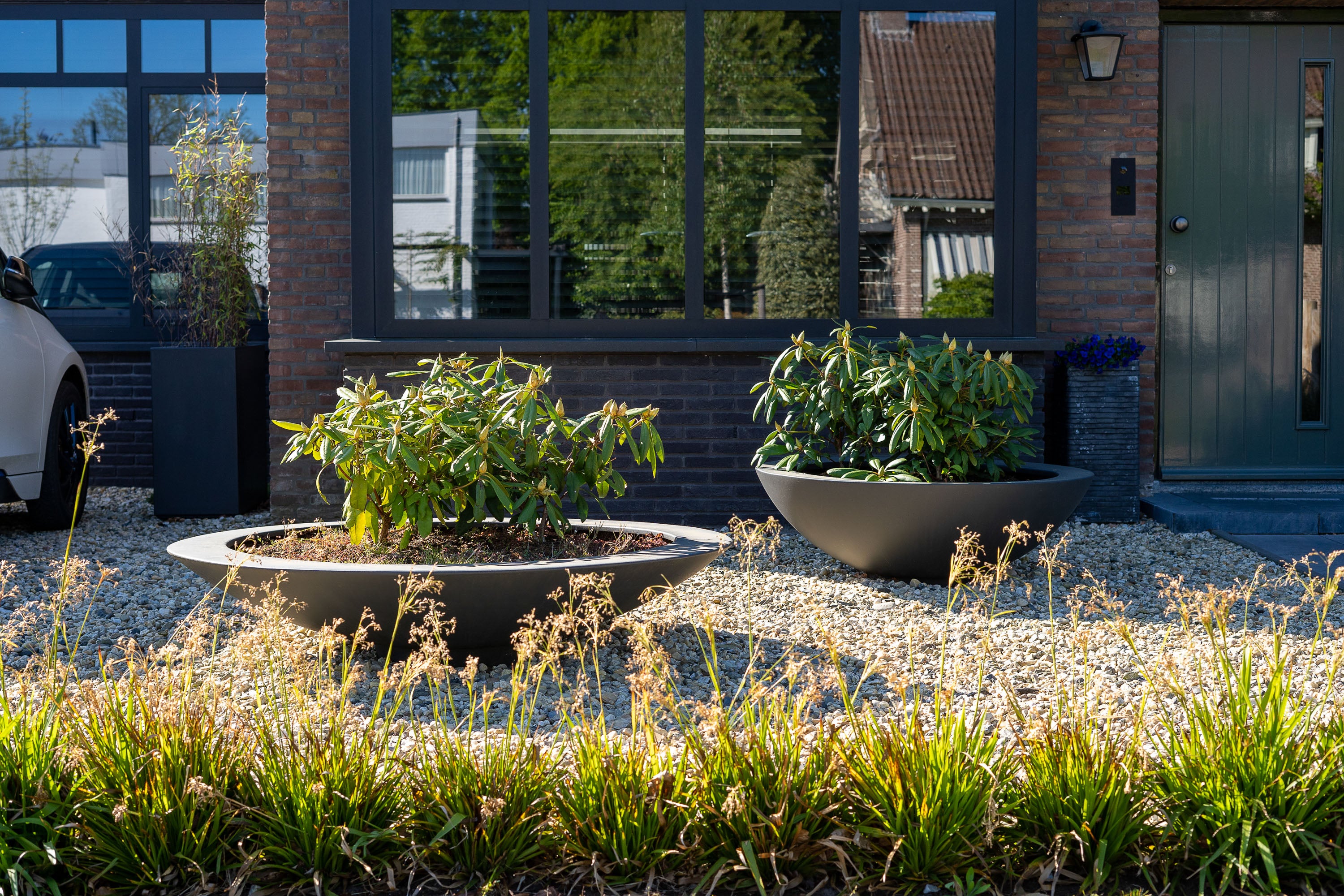 two black dish like planters with plants on gravel drive way
