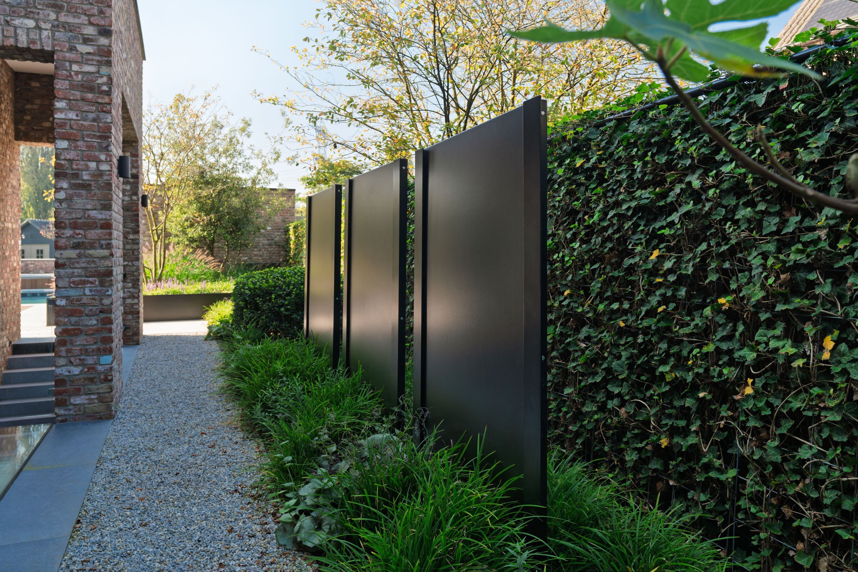 Modern black metal gate in a garden setting with greenery and a building.