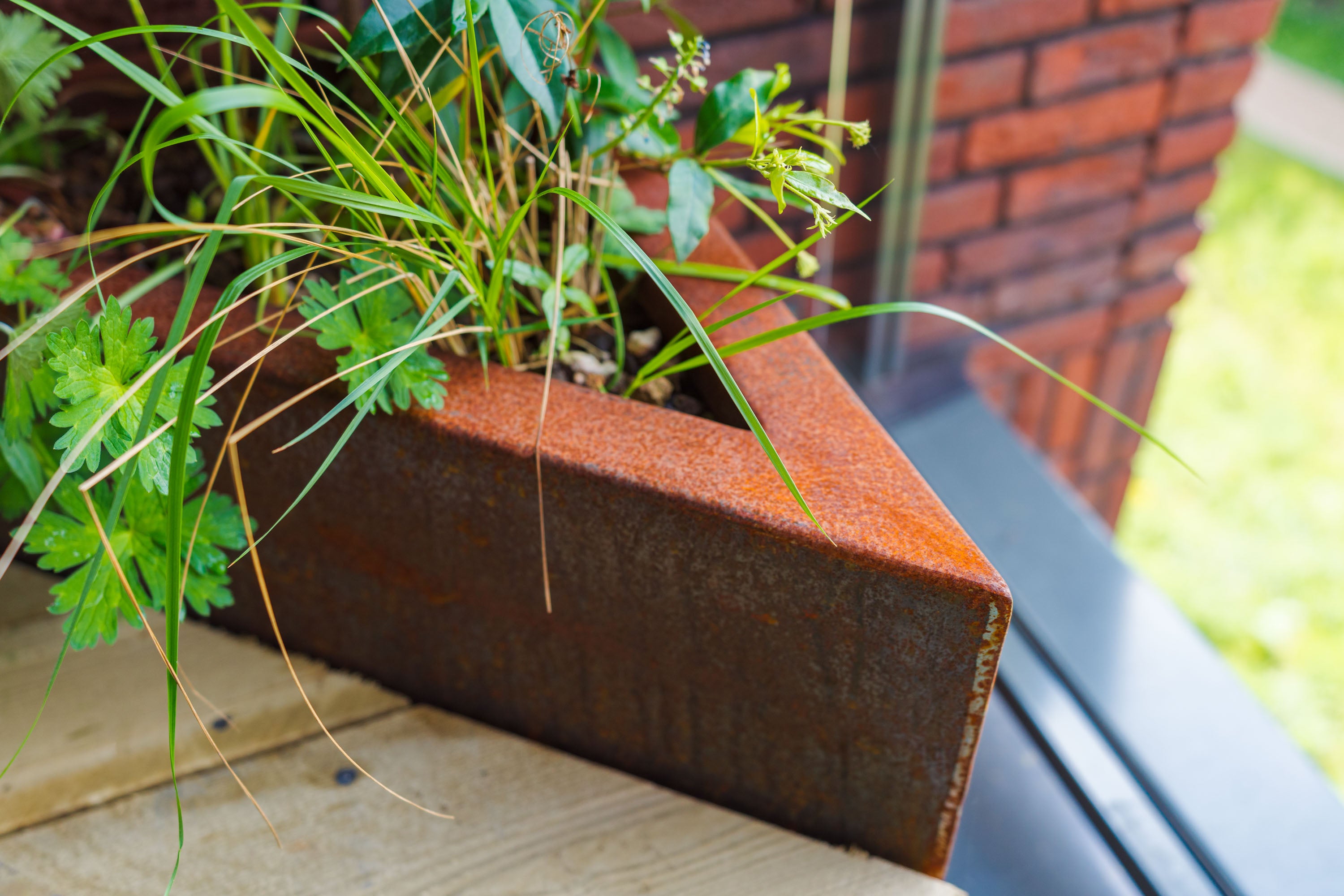 Rust-colored planter box with green plants against a brick wall.