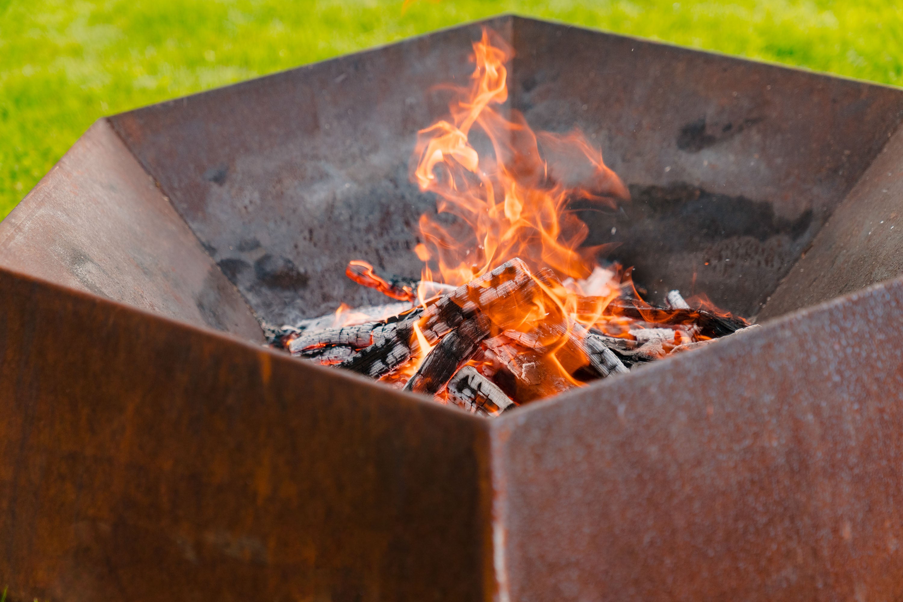Fire pit with flames and glowing embers on a grassy background
