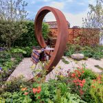 Decorative metal sculpture in a garden setting with flowers and plants.