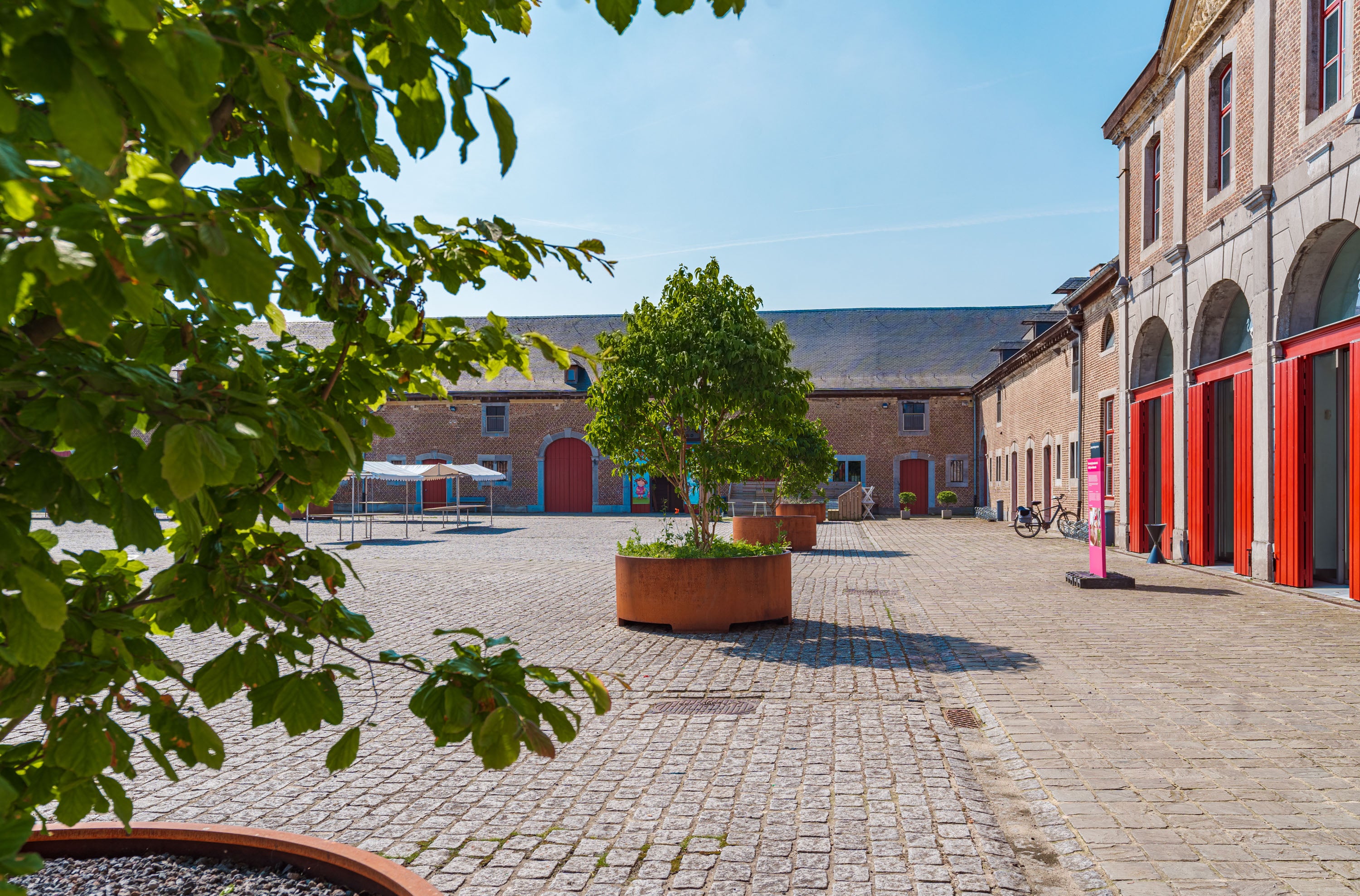 Courtyard with brick pavement, trees, and red-bricked buildings under a clear blue sky.