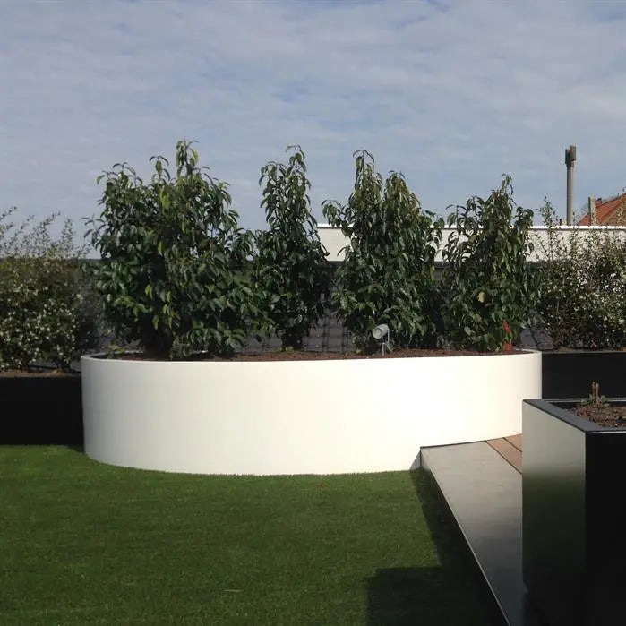 Garden with a white curved garden planter, green grass, and trees under a blue sky.