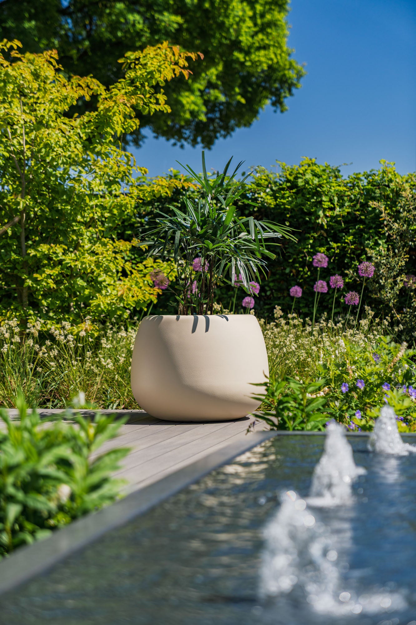 large round stone coloured planter next to water feature in garden