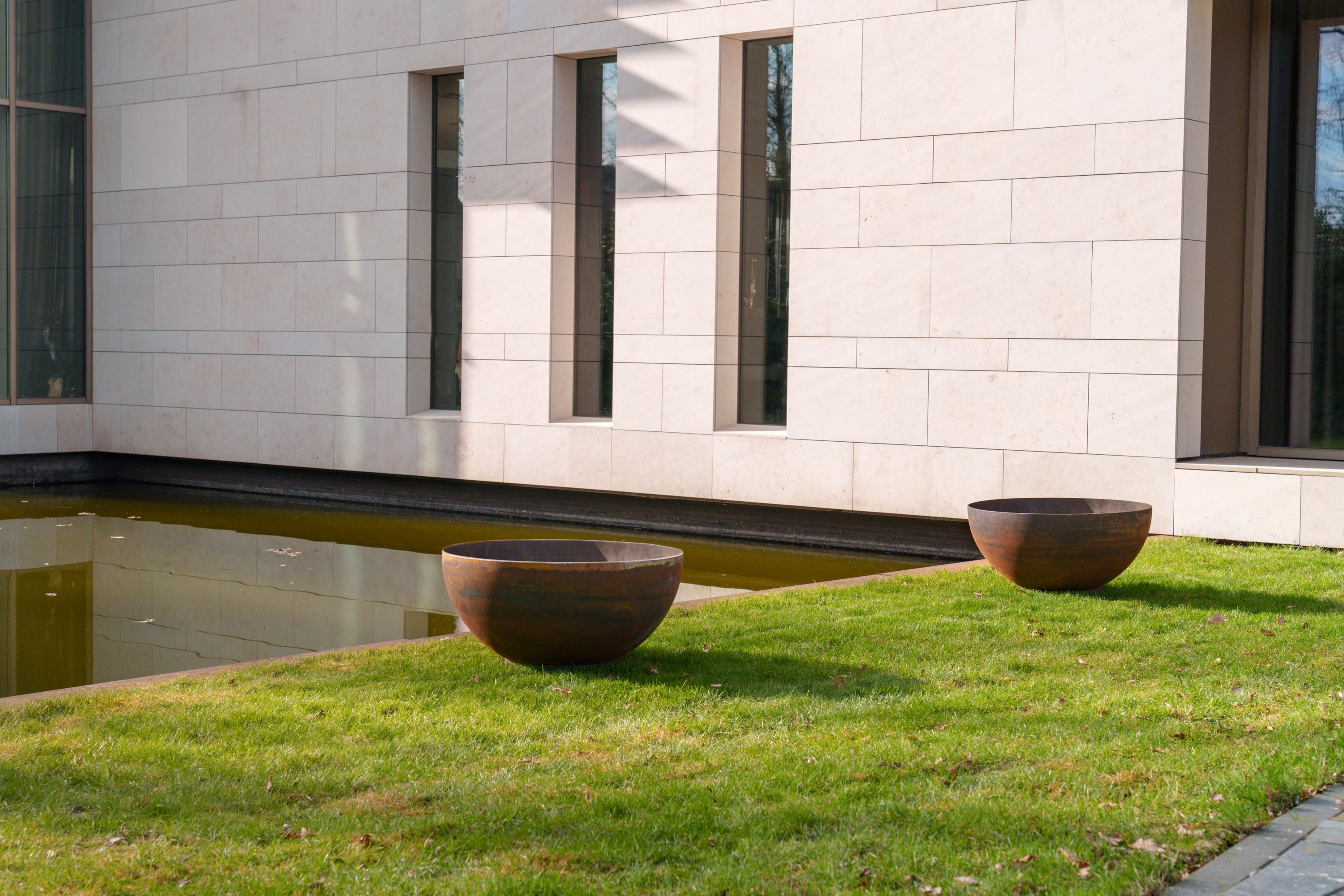 Two large metal planters on grass next to a building with a pool.