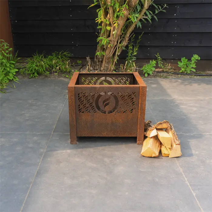 Rust-colored metal fire pit with cut-out design on a concrete patio with stacked firewood.